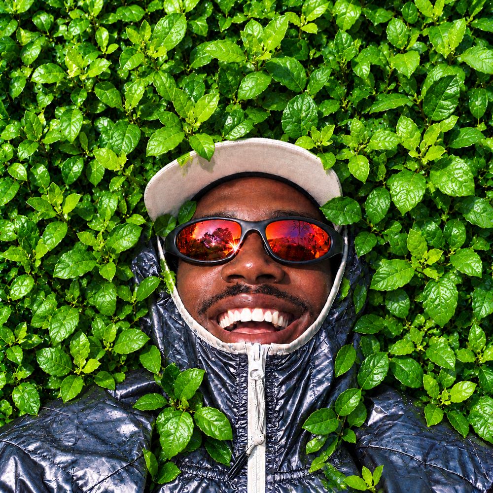 Smiling person in a cap and red sunglasses lying in green leaves